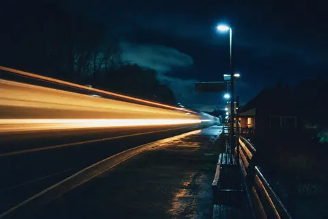 A passing night train rendered as a streak of warm light beside an empty rural platform.